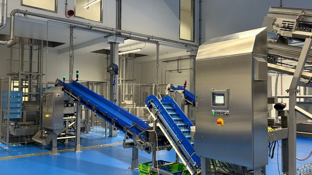 Industriële installatie voor de verwerking van verse groenten bij Hessing, met transportbanden, besturingskast en geautomatiseerde productielijn in een productieruimte. Actemium in Nederland.