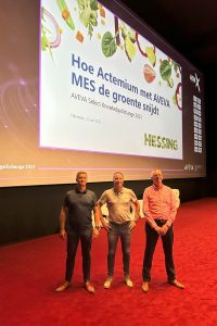 Presentatie over het MES-systeem van AVEVA voor Hessing tijdens de AVEVA Knowledge Exchange, met sprekers op het podium en projectinformatie op een groot scherm. Actemium in Nederland.