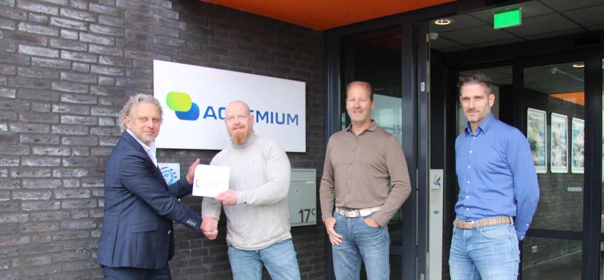 Docent van het Graafschap College en Business Unit General Managers van Actemium staan voor het Actemium-kantoor in Doetinchem tijdens de overhandiging van een gevelschild. Op de foto schudden twee personen elkaar de hand terwijl een bord van het Graafschap College wordt overhandigd. Op de achtergrond zijn het Actemium-logo en de entree van het pand zichtbaar.