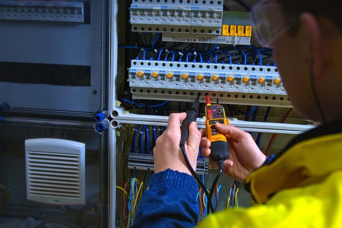 Monteur van Actemium voert met meetapparatuur een controle uit in een elektrische verdeelkast. De foto toont onderhoud en inspectie van een energievoorzieningsinstallatie, waarbij de betrouwbaarheid, veiligheid en beschikbaarheid van elektrische systemen en schakelinstallaties worden gewaarborgd.
