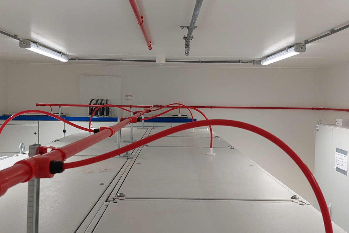Technische ruimte met rood leidingwerk voor een brandbeveiligingsinstallatie aan het plafond en elektrische aansluitingen langs de wand.