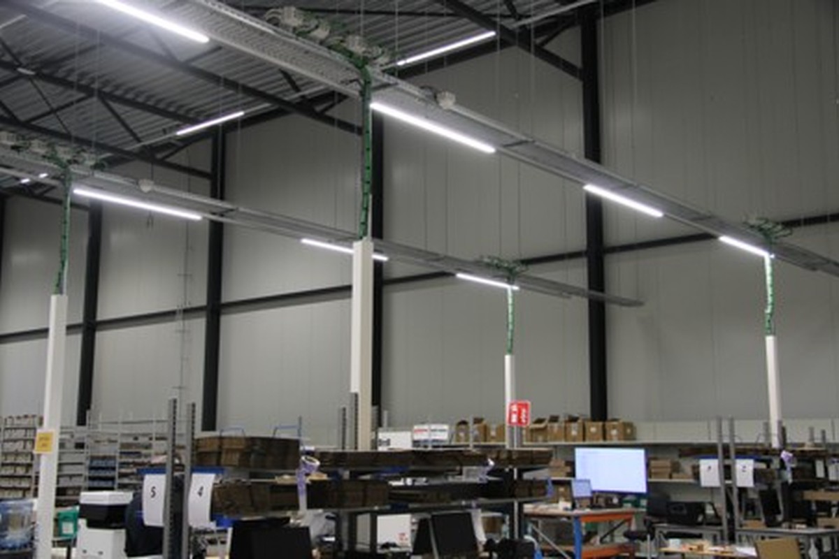 Overzicht van een bedrijfshal met industriële LED-verlichting, werkstations, stellingen en logistieke activiteiten op de werkvloer.