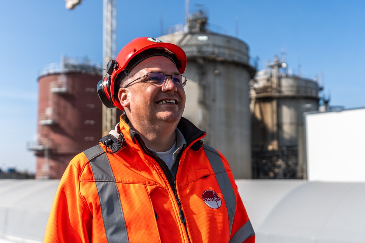Persoon in veiligheidskleding bij de industriële installaties van Omrin in Oudehaske, met vergistinginstallaties op de achtergrond.
