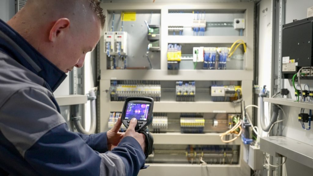 Service inspecteur aan het werk met warmtebeeldcamera bij Senefelder Misset vanuit Actemium In Doetinchem bij de klant. Thermografisch onderzoek bij paneelkast.