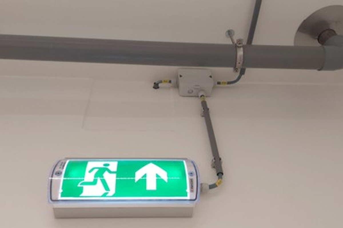 Actemium levert geïntegreerde beveiligingsinstallaties voor gebouwen en technische ruimtes. Op de afbeelding zijn rode blusgascilinders, leidingwerk, een toegangsdeur en noodverlichting te zien als onderdeel van een brandbeveiligings- en veiligheidsinstallatie.