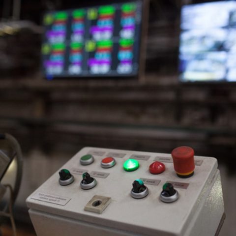 Bedieningspaneel van een industriële installatie met drukknoppen en signaleringslampen op de voorgrond. Actemium Controlsadvies helpt organisaties bij het beoordelen, verbeteren en moderniseren van besturings- en bedieningssystemen voor een betrouwbare productieomgeving.