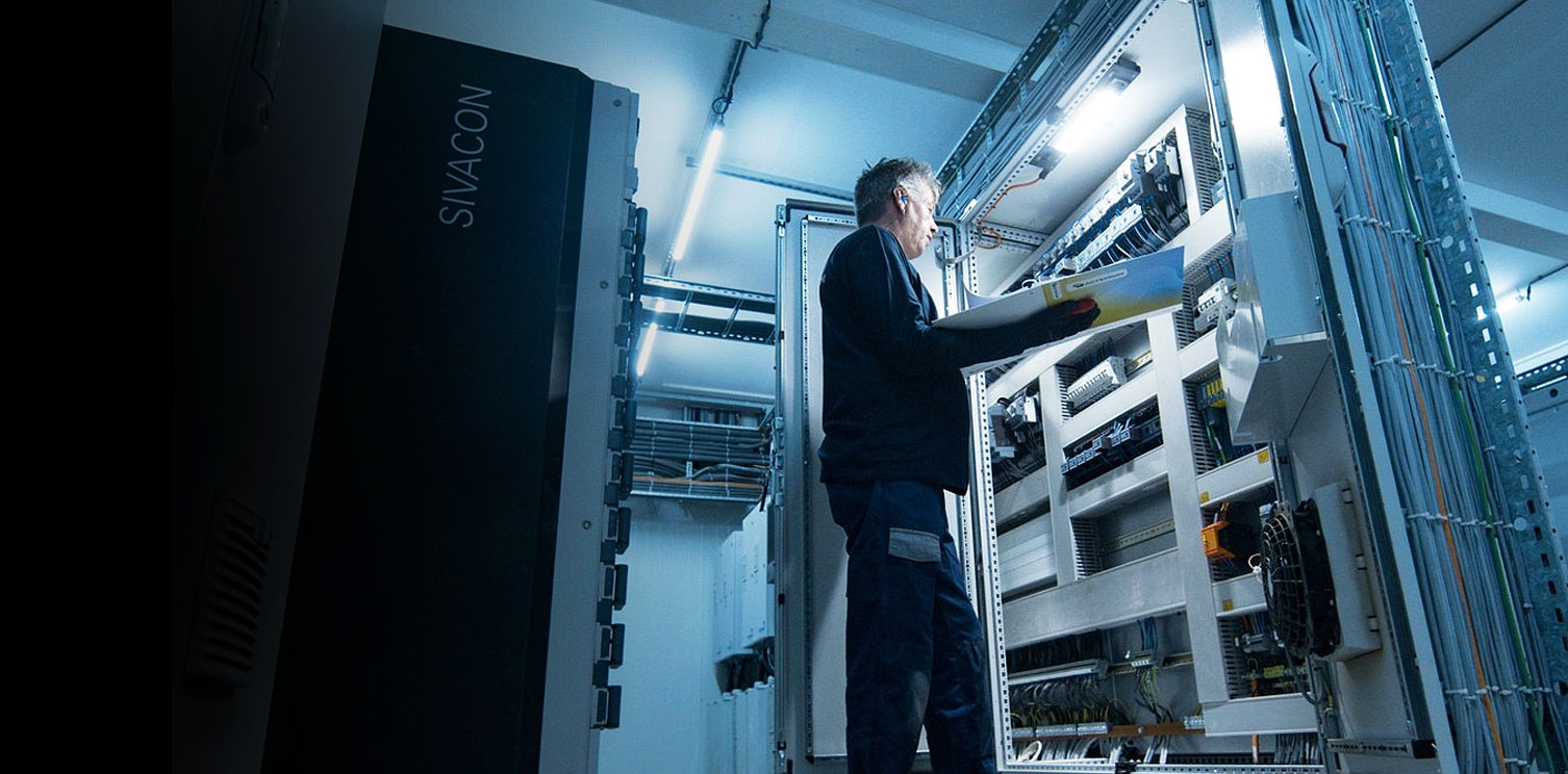 Monteur van Actemium controleert technische documentatie bij een geopende schakelkast tijdens industrieel onderhoud aan een elektrische installatie.