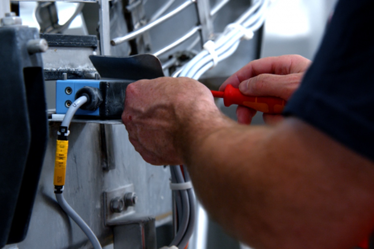 Close-up van een technicus die met een schroevendraaier werkzaamheden uitvoert aan een industriële machine met bekabeling en elektrische componenten.