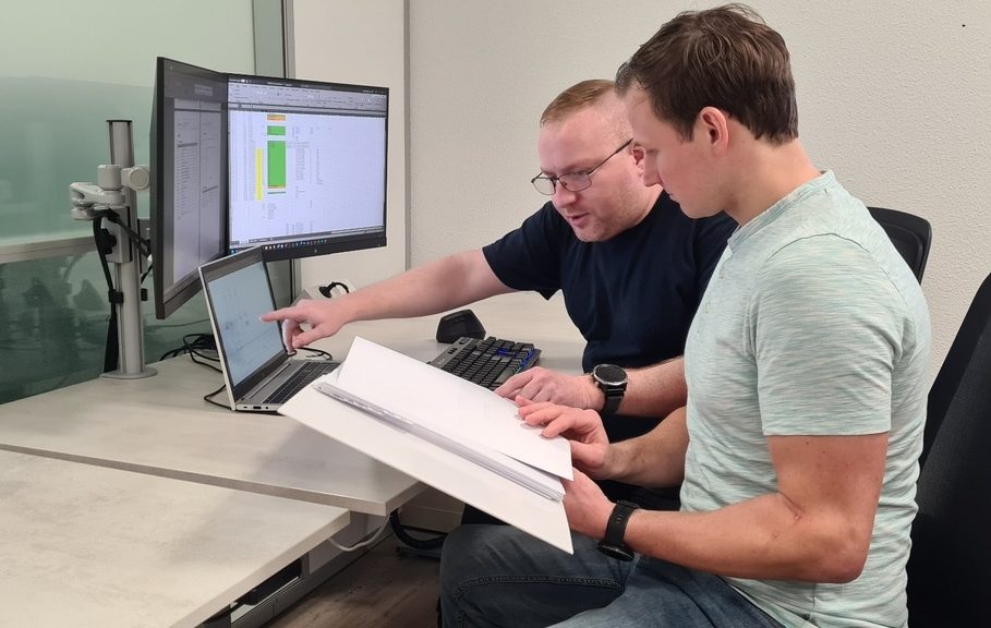 Twee experts bespreken projectgegevens en controleren technische documentatie op laptop en monitoren in een kantooromgeving. Actemium in Nederland.