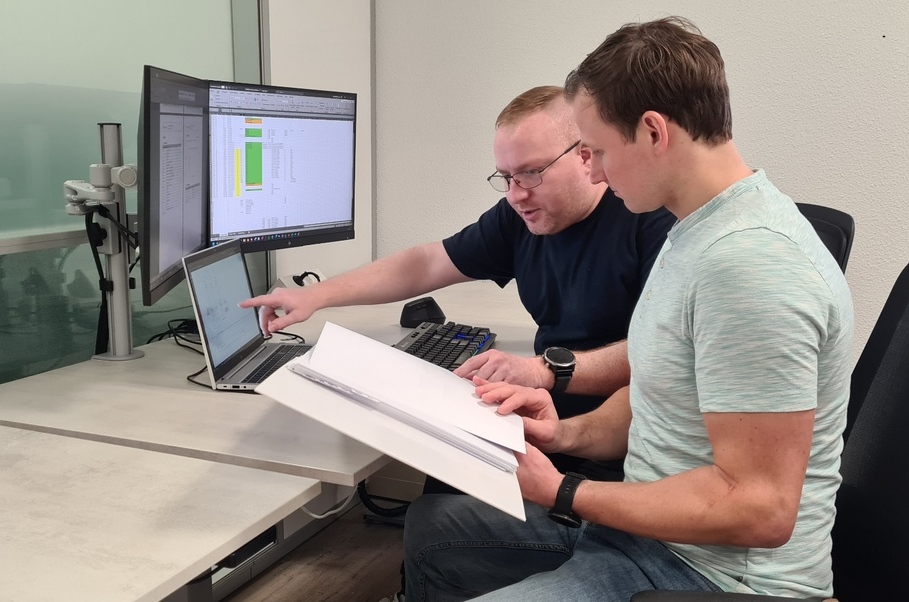 Twee experts bespreken projectgegevens en controleren technische documentatie op laptop en monitoren in een kantooromgeving. Actemium in Nederland.