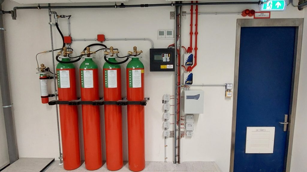 Actemium Building Technologies brandmeldinstallaties en ontruimingsalarminstallaties in een technische ruimte met blusinstallatie, detectiesystemen, leidingwerk en veiligheidsvoorzieningen voor brandveiligheid.