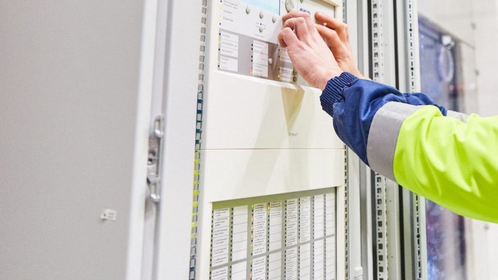 Monteur bedient een brandmeldcentrale van Actemium Building Technologies voor brandmeldinstallaties en ontruimingsalarminstallaties, met focus op inspectie, beheer en monitoring van brandveiligheidssystemen.