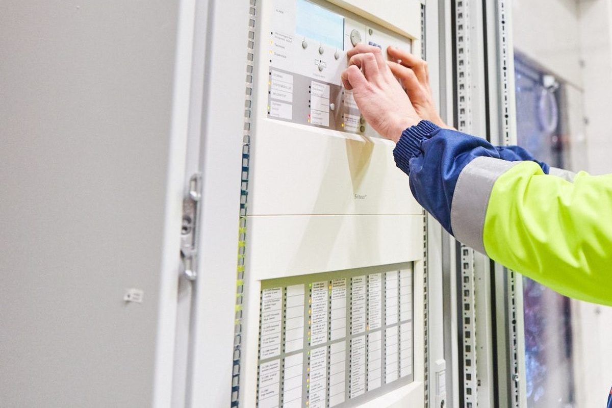 Monteur bedient een brandmeldcentrale van Actemium Building Technologies voor brandmeldinstallaties en ontruimingsalarminstallaties, met focus op inspectie, beheer en monitoring van brandveiligheidssystemen.