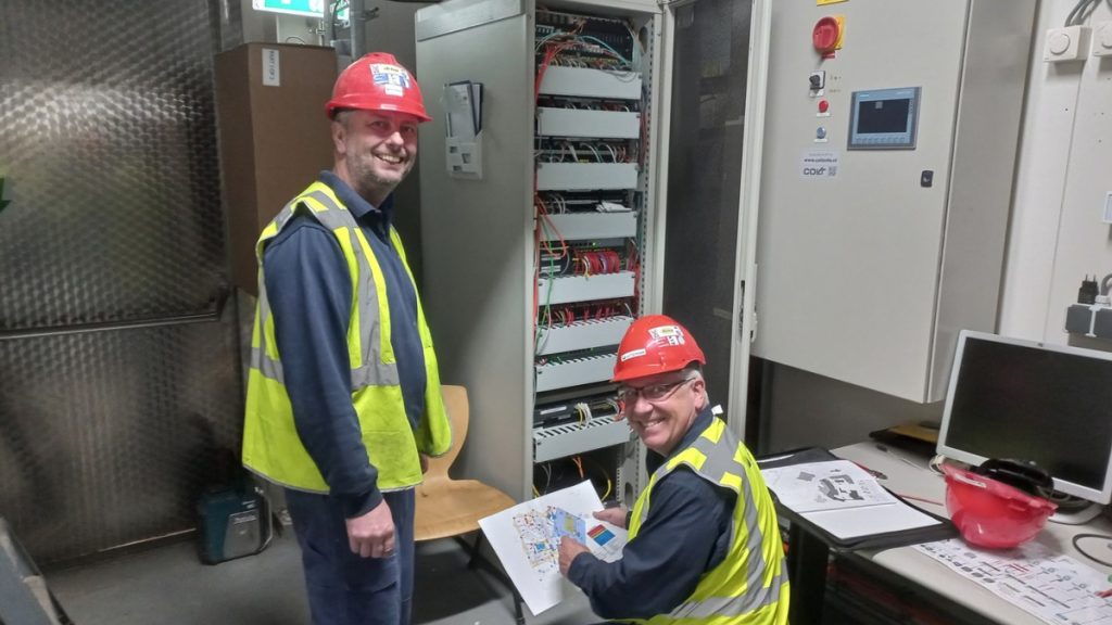 Technische specialisten controleren en onderhouden installaties in een server- of technische ruimte. Actemium Building Technologies waarborgt de betrouwbaarheid van brandmeldinstallaties in kritische omgevingen.