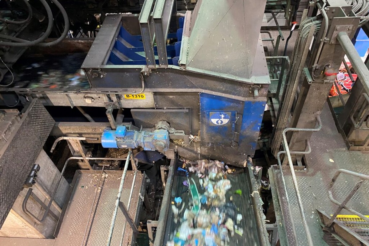 Industriële sorteerlijn voor afvalverwerking met transportbanden, loopbruggen en installaties voor mechanische afvalscheiding in een verwerkingshal.